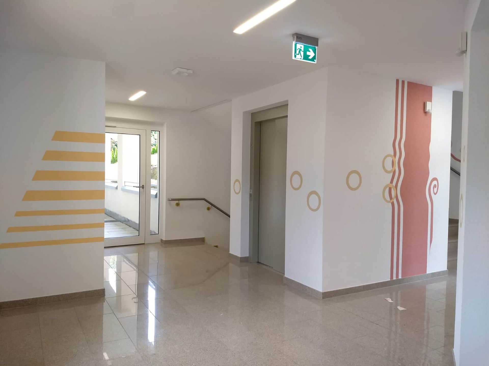 Heller Flur mit modernen Wandmalereien und Aufzug.