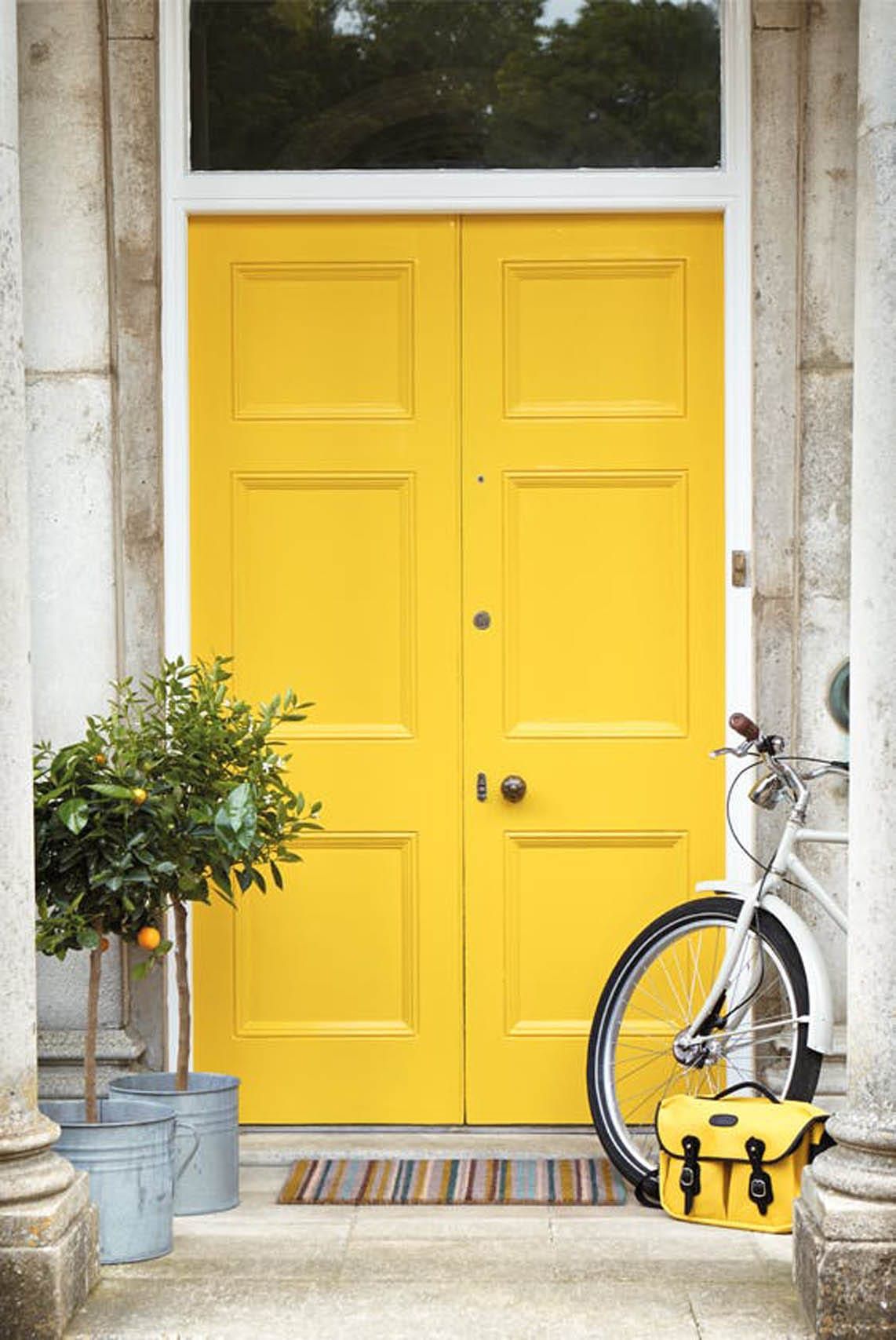 Helle gelbe Tür mit Fahrrad und Pflanzen.