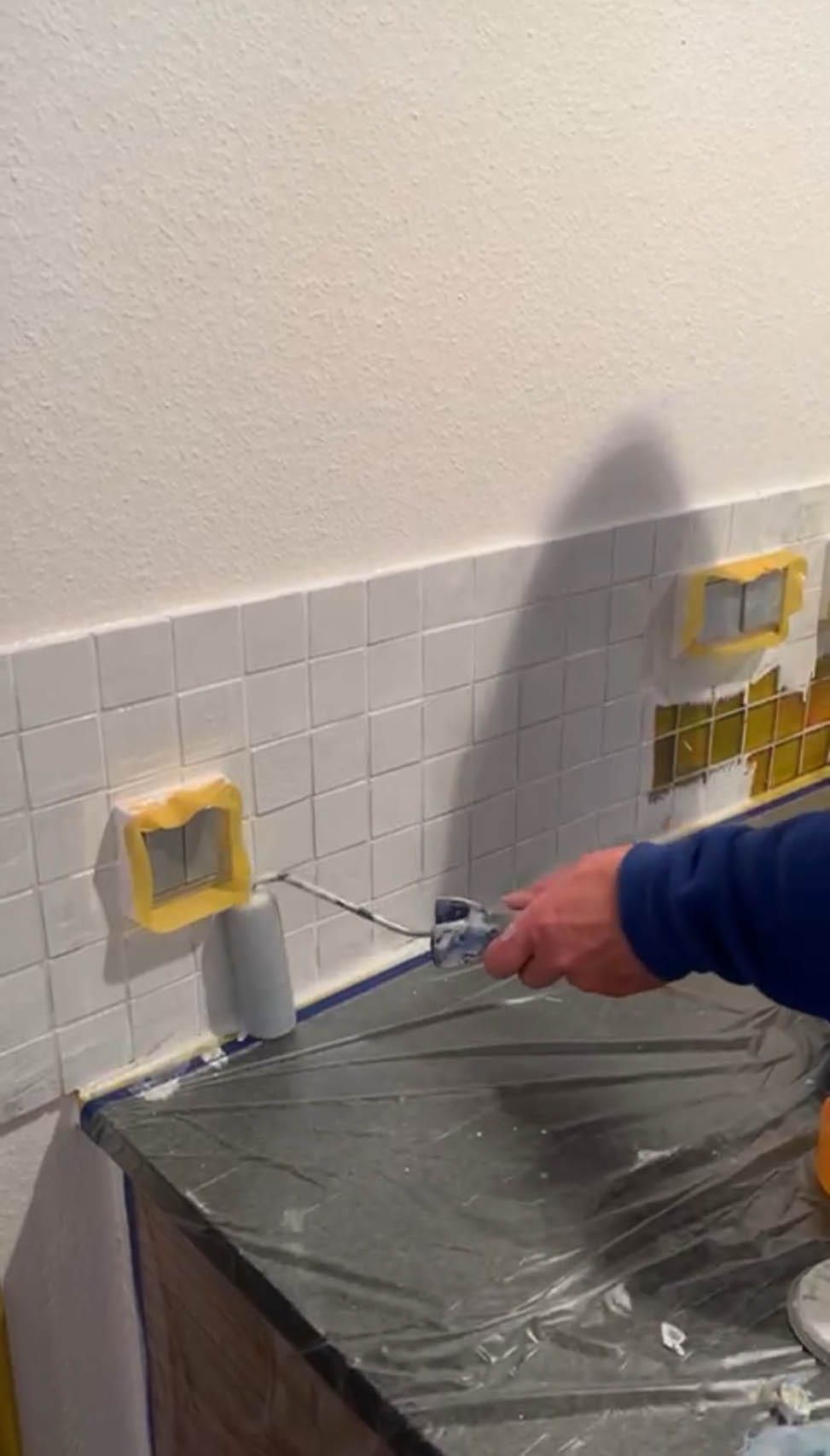 Mann streicht Wandfliesen mit Farbroller