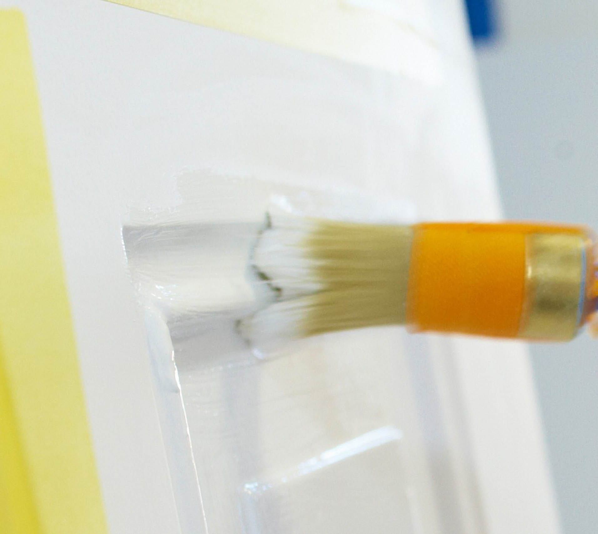 Pinsel streicht weiße Farbe auf eine Oberfläche