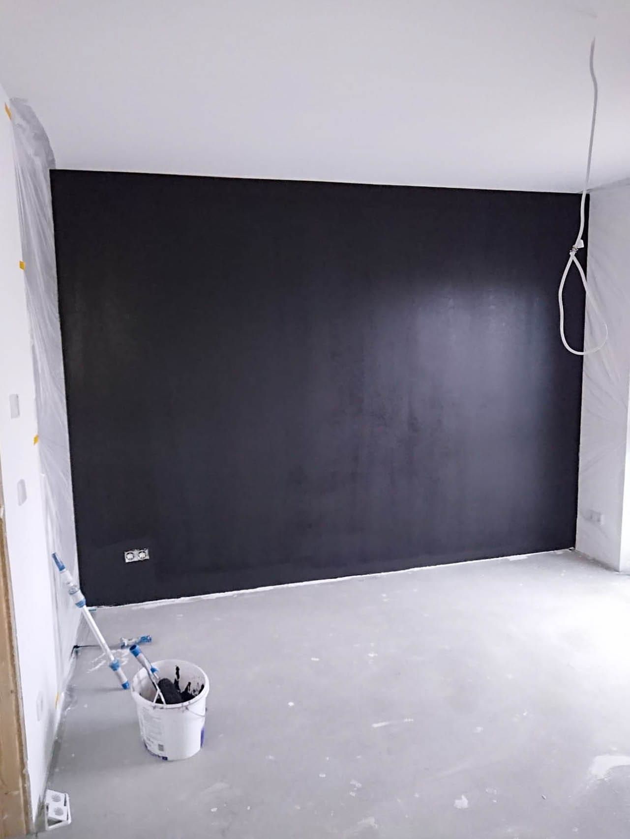 Leerraum mit schwarzer Wand und Malerutensilien.
