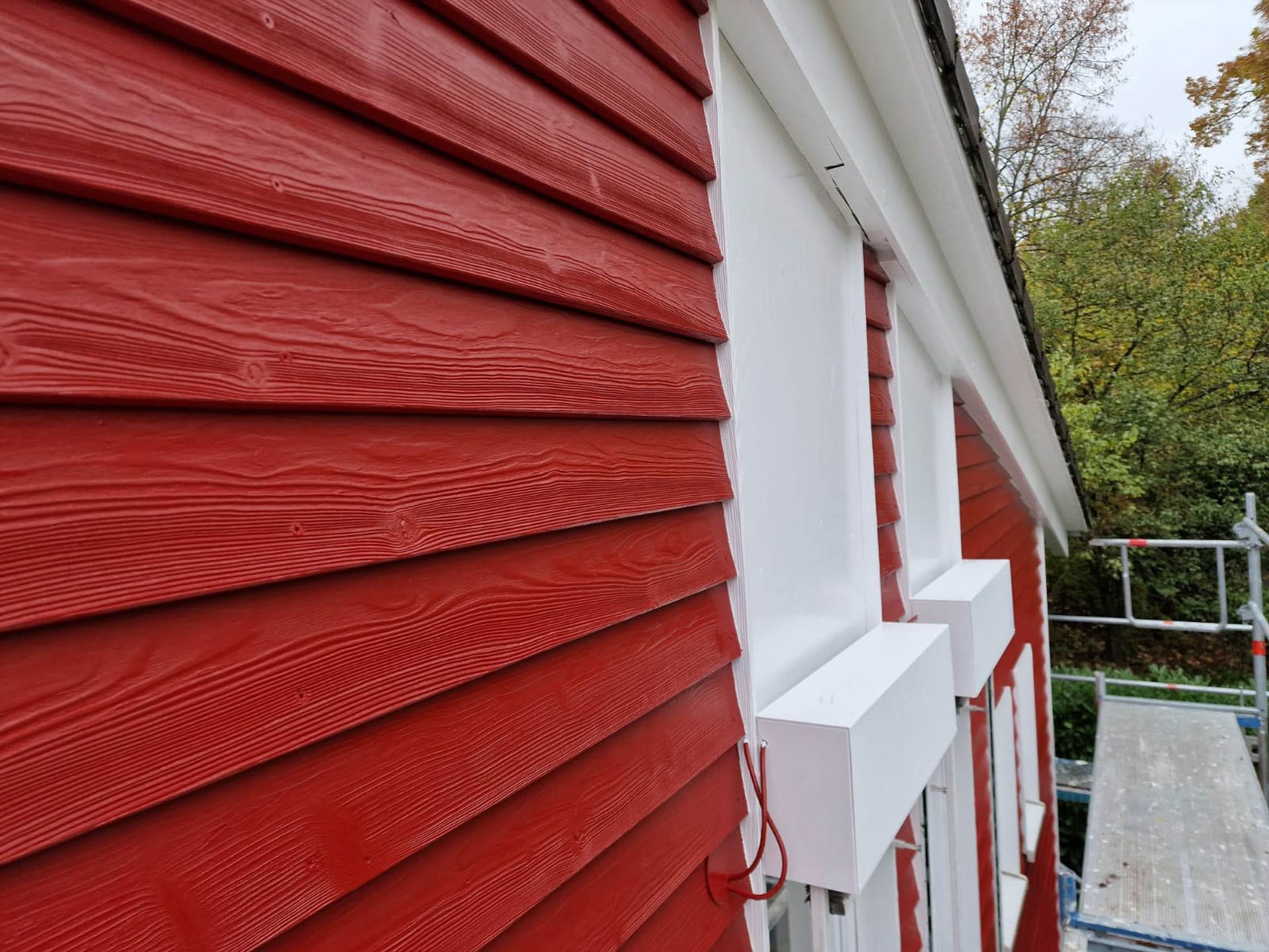 Rote Holzfassade mit weißen Fenstern und Rahmen.