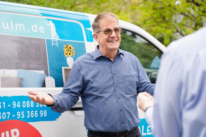 Mann spricht vor einem Auto mit Werbung.