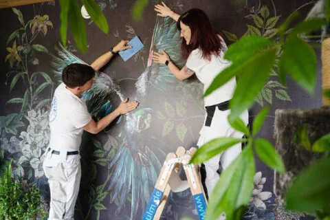 Zwei Personen montieren Wandtapete mit Vogelmotiv.